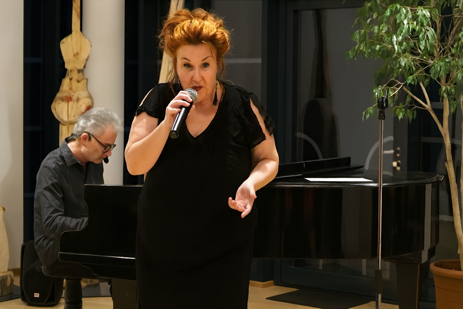 Frau Sonntag steht vor einem Klavier und singt in ein Mikrofon