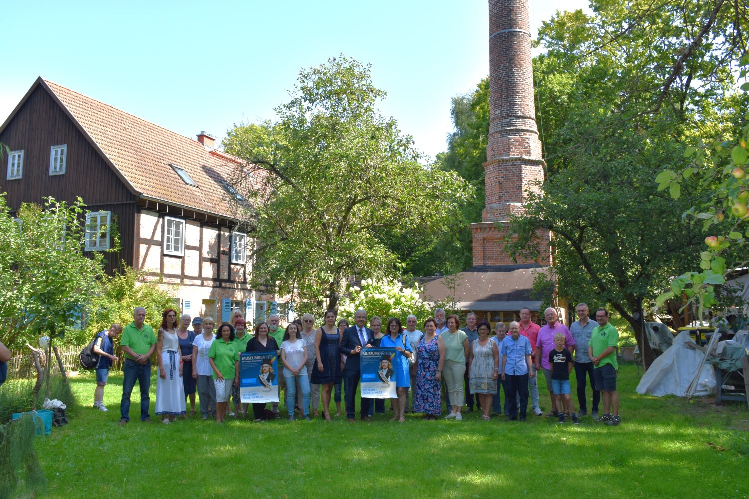 Menschengruppe stehen in einer Reihe mit zwei Plakaten von der Museumsnacht im Landkreis Spree Neiße